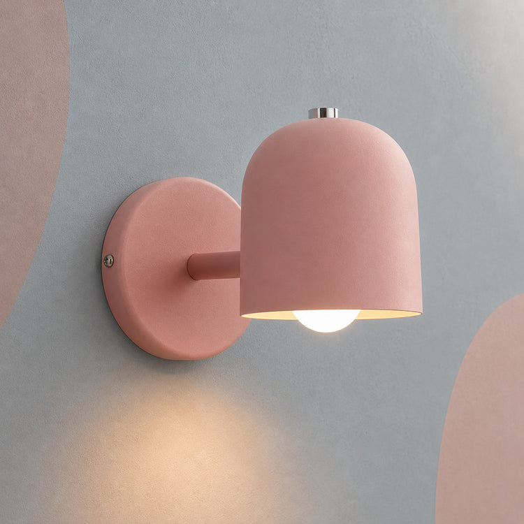 Pink dome bedside wall lamp lit warm on a blue-gray wall