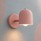 Pink dome bedside wall lamp lit warm on a blue-gray wall