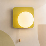 A modern square wall sconce with a glowing circular light in the center, mounted on a beige wall with abstract color-blocked shapes. The fixture has a mustard yellow outer frame and a pull chain with a small wooden knob.