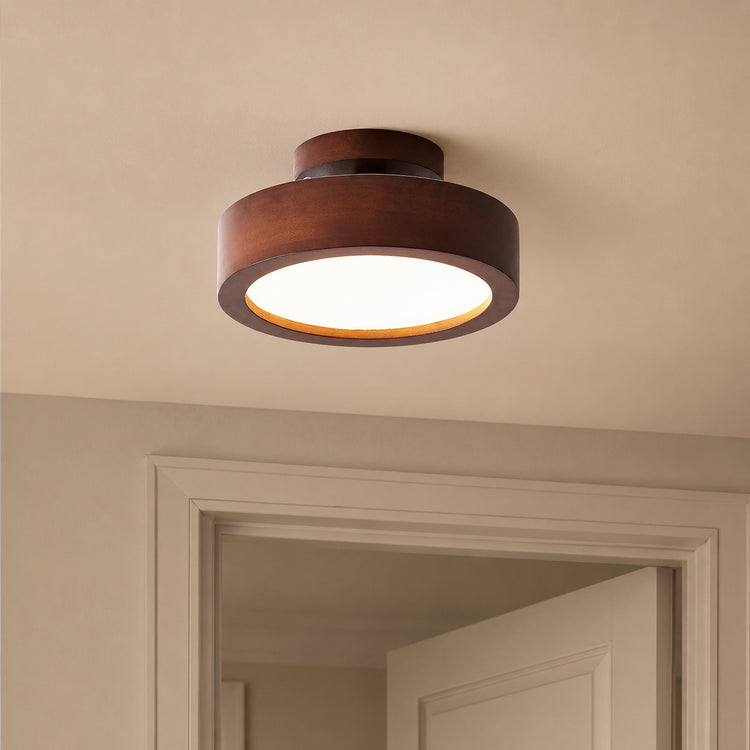 A modern semi-flush mount ceiling light with a dark brown wood-grain outer ring and a glowing white frosted glass shade, installed on a beige ceiling above a doorway.
