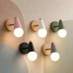 Five lit globe vanity sconces in macaron colors with iron and wood backplates on a pastel color-block wall