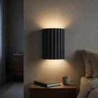 Charcoal fluted wall sconce lit beside a bed above a walnut nightstand at night