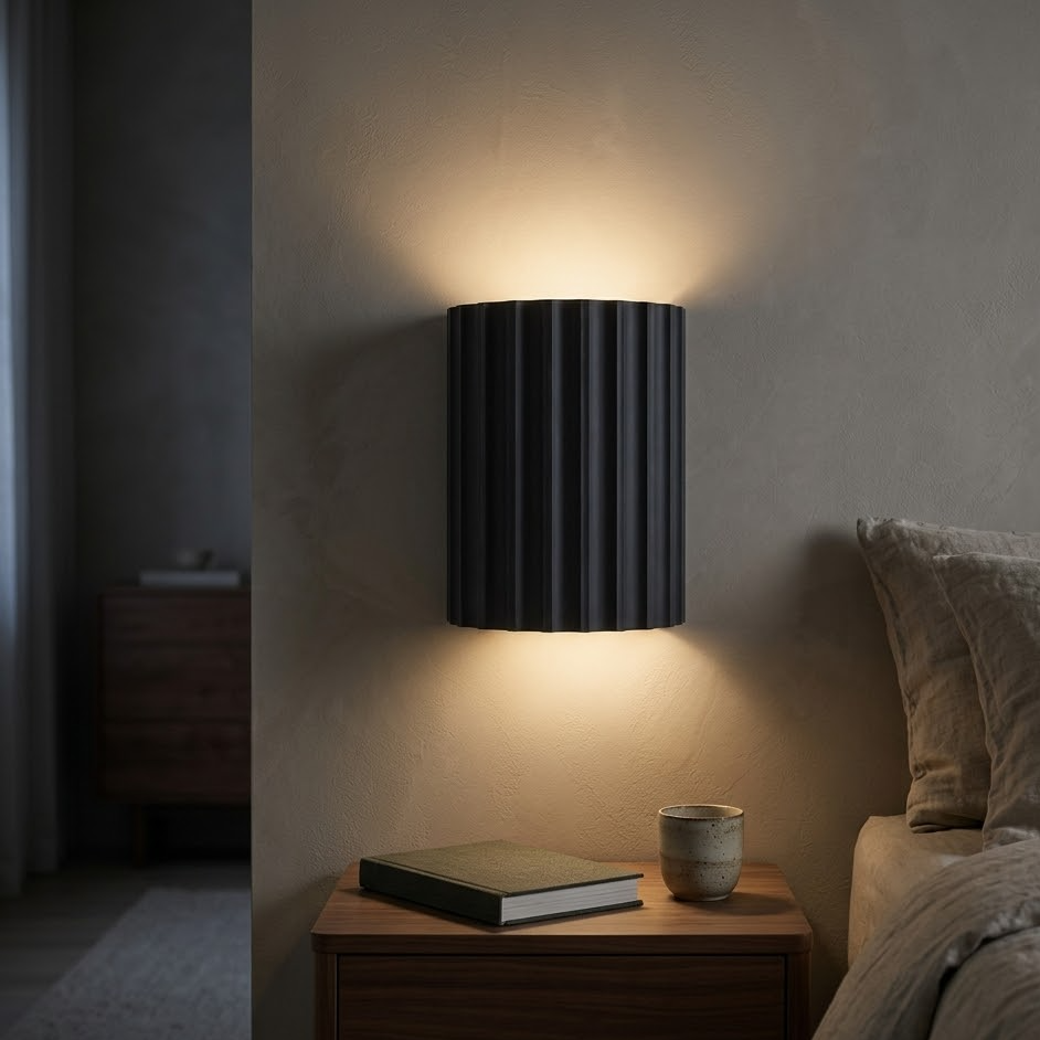 Charcoal fluted wall sconce lit beside a bed above a walnut nightstand at night