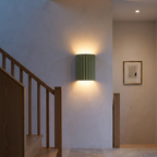 Olive green fluted wall sconce washing light up a stair landing wall