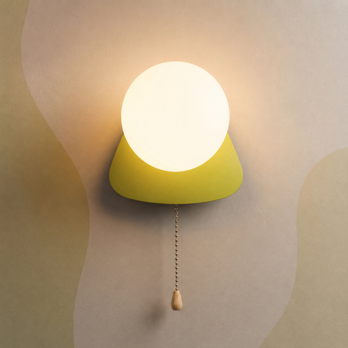 A modern wall sconce with a glowing white spherical bulb and a bright yellow-green conical shade, mounted on a beige wall with abstract wavy patterns. A pull chain with a small wooden knob hangs below.