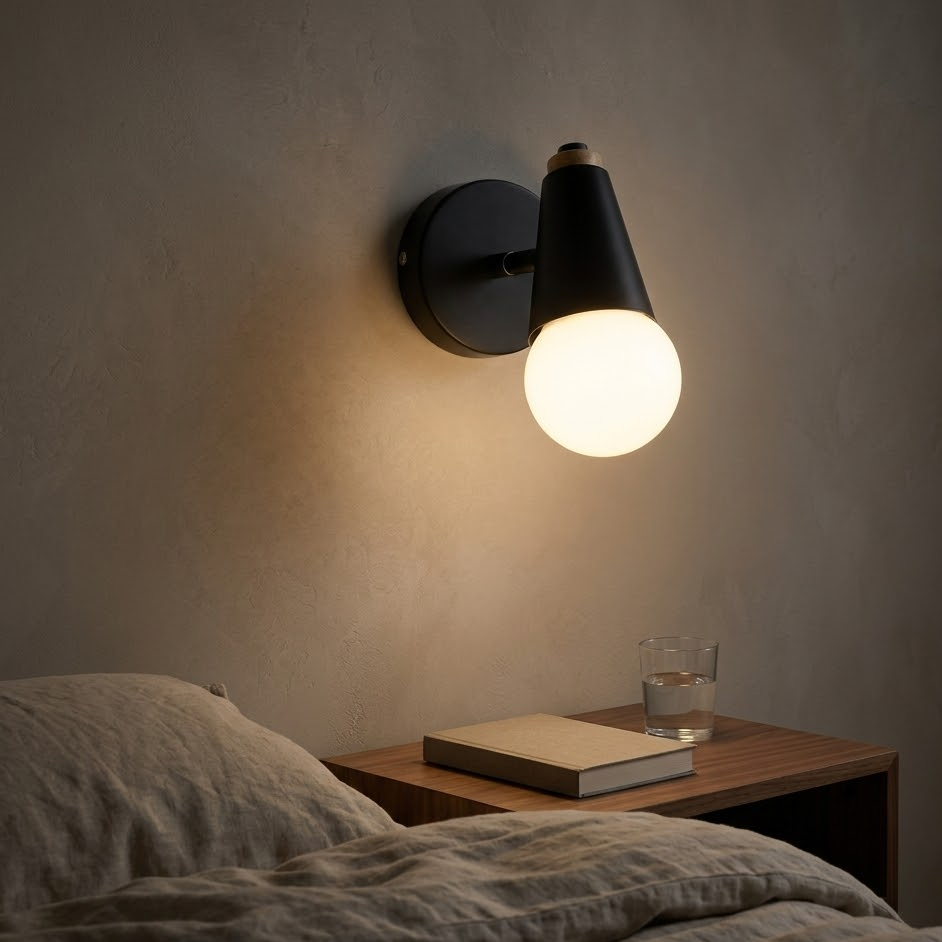 Black globe wall sconce lit at night above a walnut nightstand beside a bed
