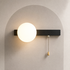 Matte black bar globe wall sconce with the globe on the left and pull chain switch