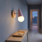 Pink globe wall sconce lit above an oak console table in a hallway at dusk