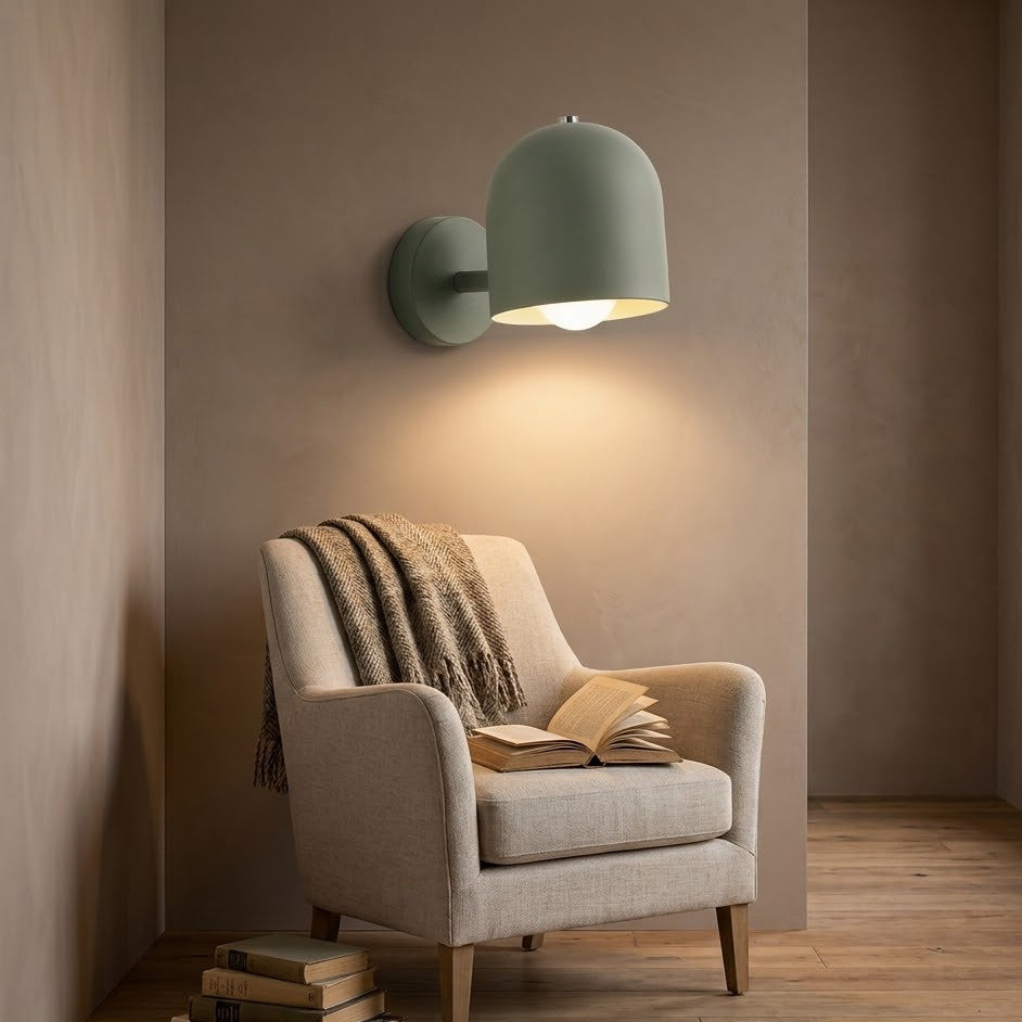 Green dome wall sconce lit above a linen armchair in a reading nook
