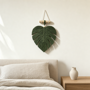 Macrame Monstera Leaf Wall Hanging, 25 cm, 4 Colors hung on the wall above a bed