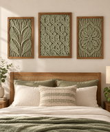 Three framed vertical wall art panels with textured botanical and geometric designs in sage green and beige tones, displayed above a wooden bed with neutral bedding in a styled bedroom setting.