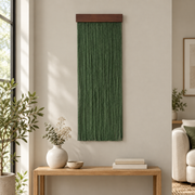 Green fringe wall hanging above a light wood console with a vase in a living room