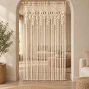 Cream macrame door curtain hung in an arched living room opening with light beyond