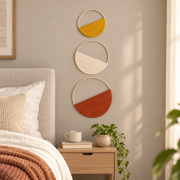 Three woven hoops on a bedroom wall above a wooden bedside table with a mug and books