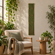 Olive macrame banner beside an armchair and plants in a reading corner