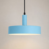 A modern pendant light with a wide, shallow circular shade in light blue, a matching blue cylindrical neck, a black hanging cord, and a warm white interior glow, set against a plain beige background.