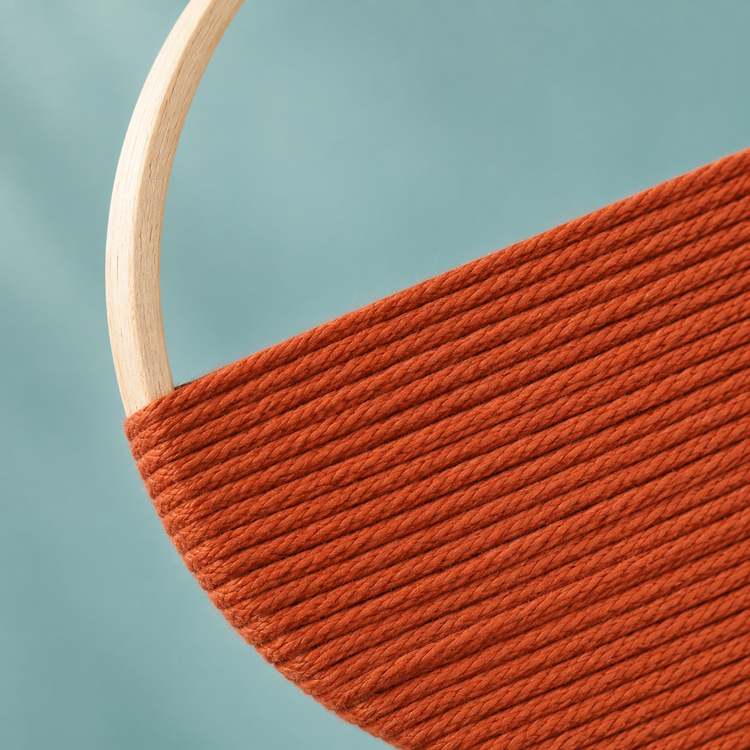 Close view of rust yarn rows meeting the pale wooden hoop edge of the woven wall art