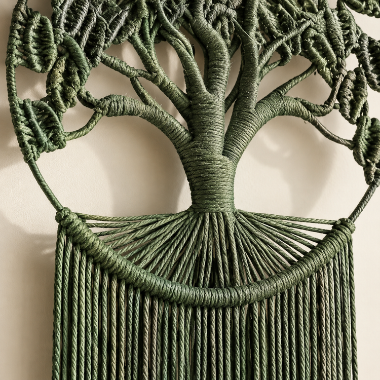 A green macrame wall hanging shaped like a tree, with a wrapped trunk and branches, leafy canopy, and long fringe hanging below, shown against a plain light background.