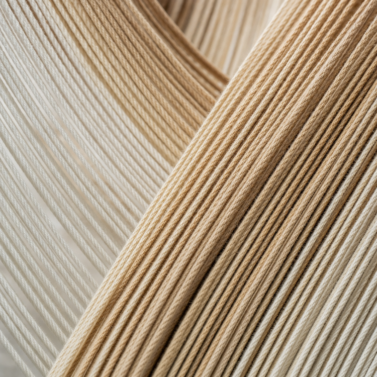 Close-up of woven rope or cord material in warm beige and off-white tones, arranged in layered diagonal folds.