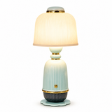 A table lamp with a ribbed ceramic body in pale aqua and dark gray, featuring gold-tone metal trim and a glowing pleated shade, shown on a white background.