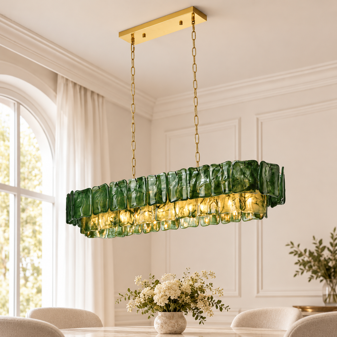 A dark green glass linear chandelier hangs from gold-toned chains above a dining table beside an arched window.