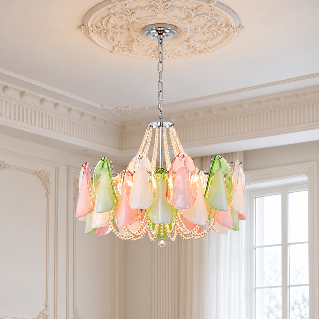 A decorative chandelier hanging from a ornate ceiling medallion in a bright, classic room. The chandelier features multiple translucent glass flower-like shades in pastel pink, light green, and white, accented by strands of white bead pearls and a silver-toned chain.