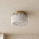 A modern flush-mount ceiling light with a cylindrical white marble shade and a brushed brass top ring, mounted on a textured beige plaster ceiling.