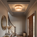 Cream alabaster flush mount light glows beneath a coffered entryway ceiling beside a staircase and wooden front door.