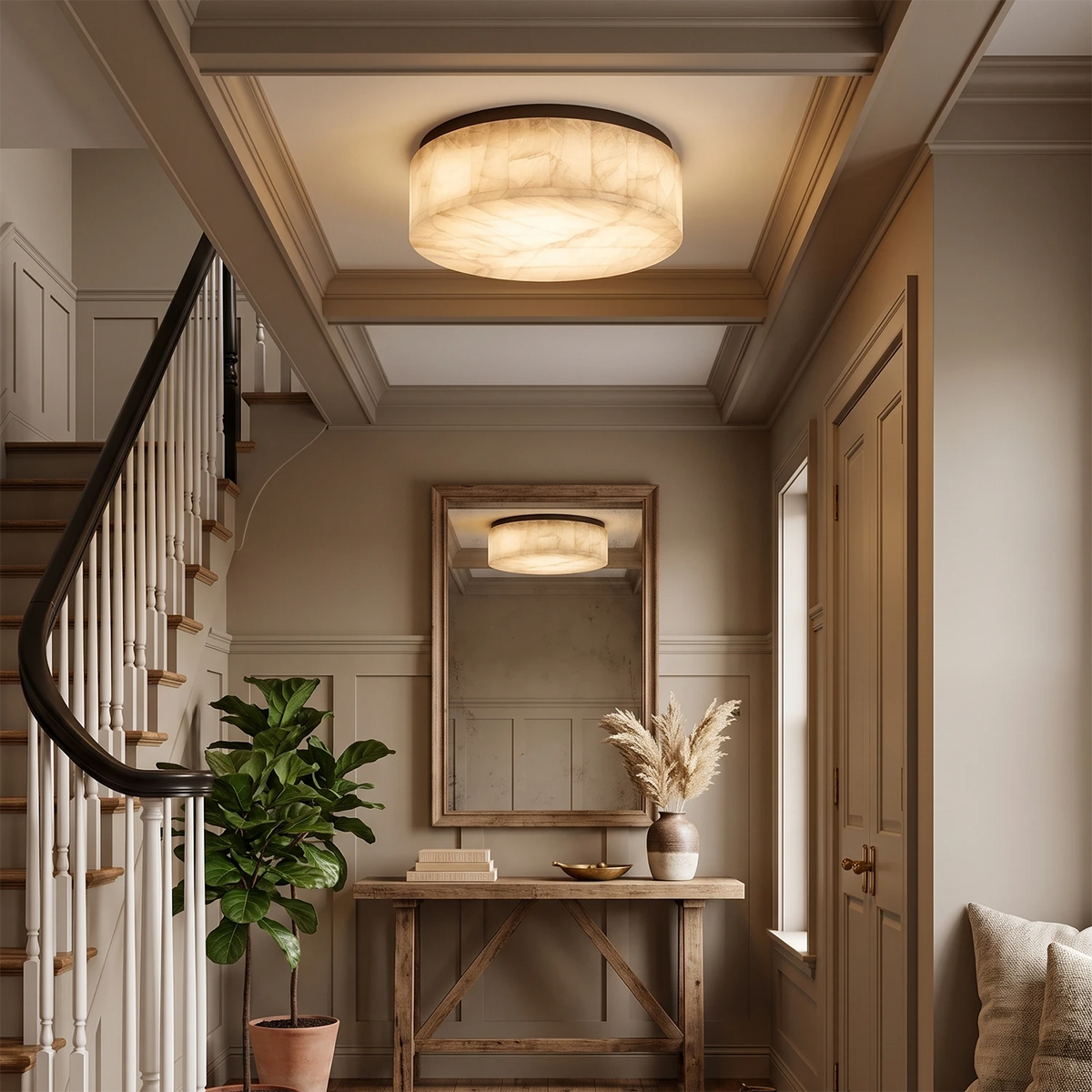 A modern flush-mount ceiling light with a textured, linen-like drum shade in warm cream and beige tones, glowing in a beautifully styled entryway with a staircase, console table, and mirror.