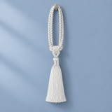 A white braided rope tassel ornament hanging against a soft light blue background.