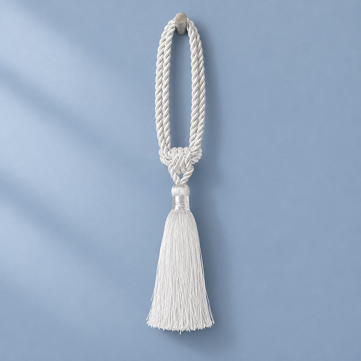 A white braided rope tassel ornament hanging against a soft light blue background.