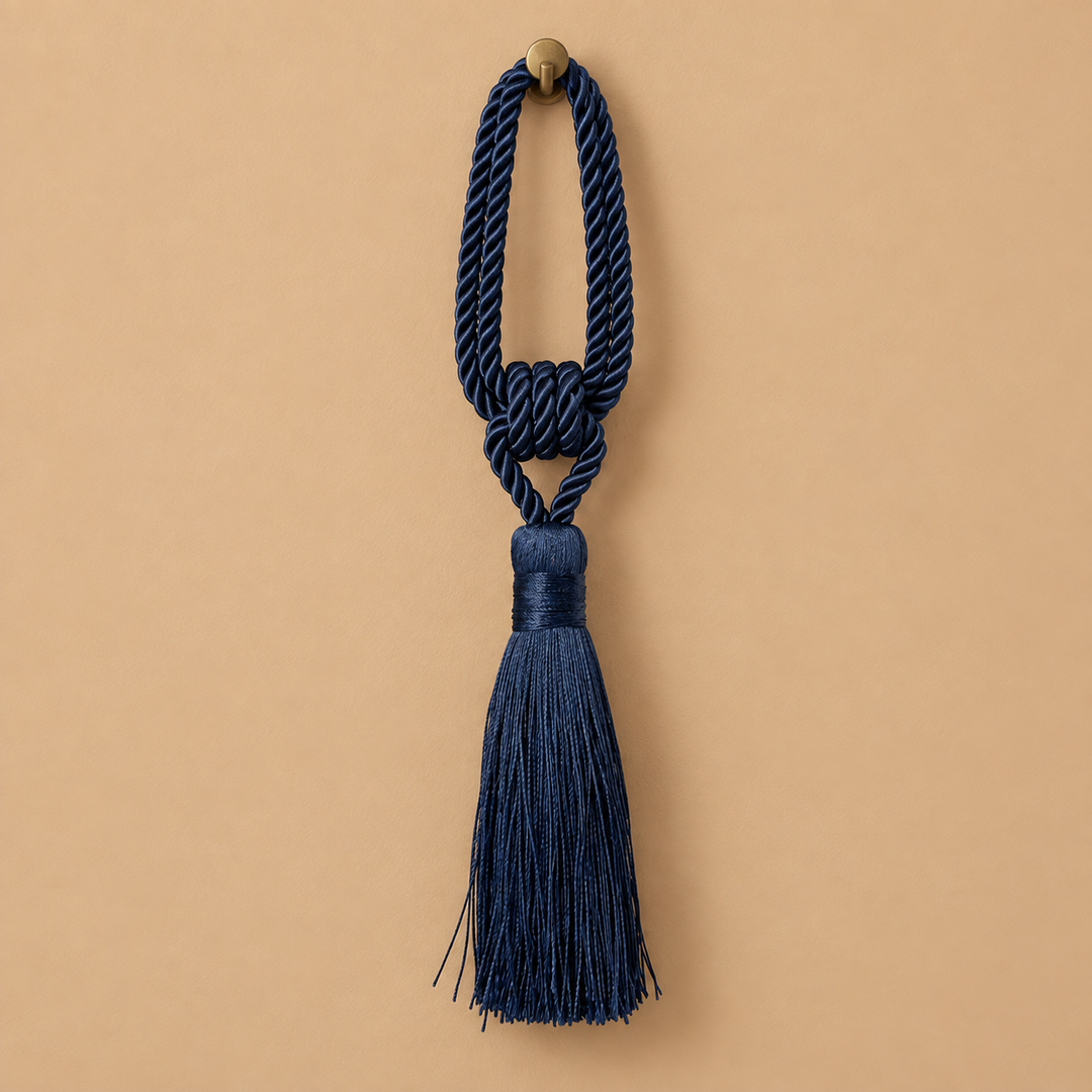 A navy blue decorative tassel with a knotted cord loop and a small round brass-tone finial, centered on a warm beige background.
