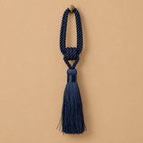 A navy blue decorative tassel with a knotted cord loop and a small round brass-tone finial, centered on a warm beige background.