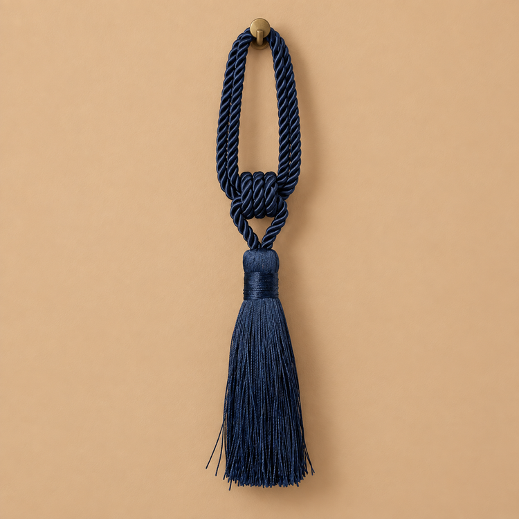 A navy blue decorative tassel with a knotted cord loop and a small round brass-tone finial, centered on a warm beige background.