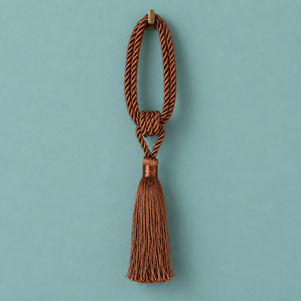 A brown braided rope tassel ornament with a knotted center and a long hanging tassel, shown against a solid teal background.