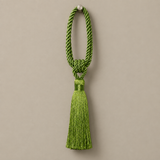 A bright green ceremonial tassel with a braided cord loop and a matching tassel, hanging against a solid taupe background.
