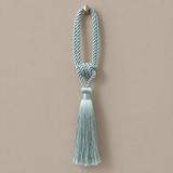 A light blue-green twisted rope tassel with a decorative knot and a matching tassel, hanging from a small metal hook against a solid beige background.