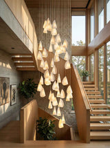 Modern chandelier hanging in a staircase with large windows and plants.