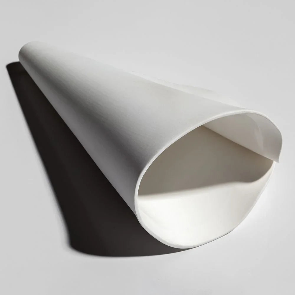 A white porcelain chandelier shade rests sideways on a pale surface, showing its overlapping folded edges and open interior.