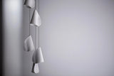 Unlit white chandelier shades hang vertically at staggered heights on thin dark cords against a gray wall.