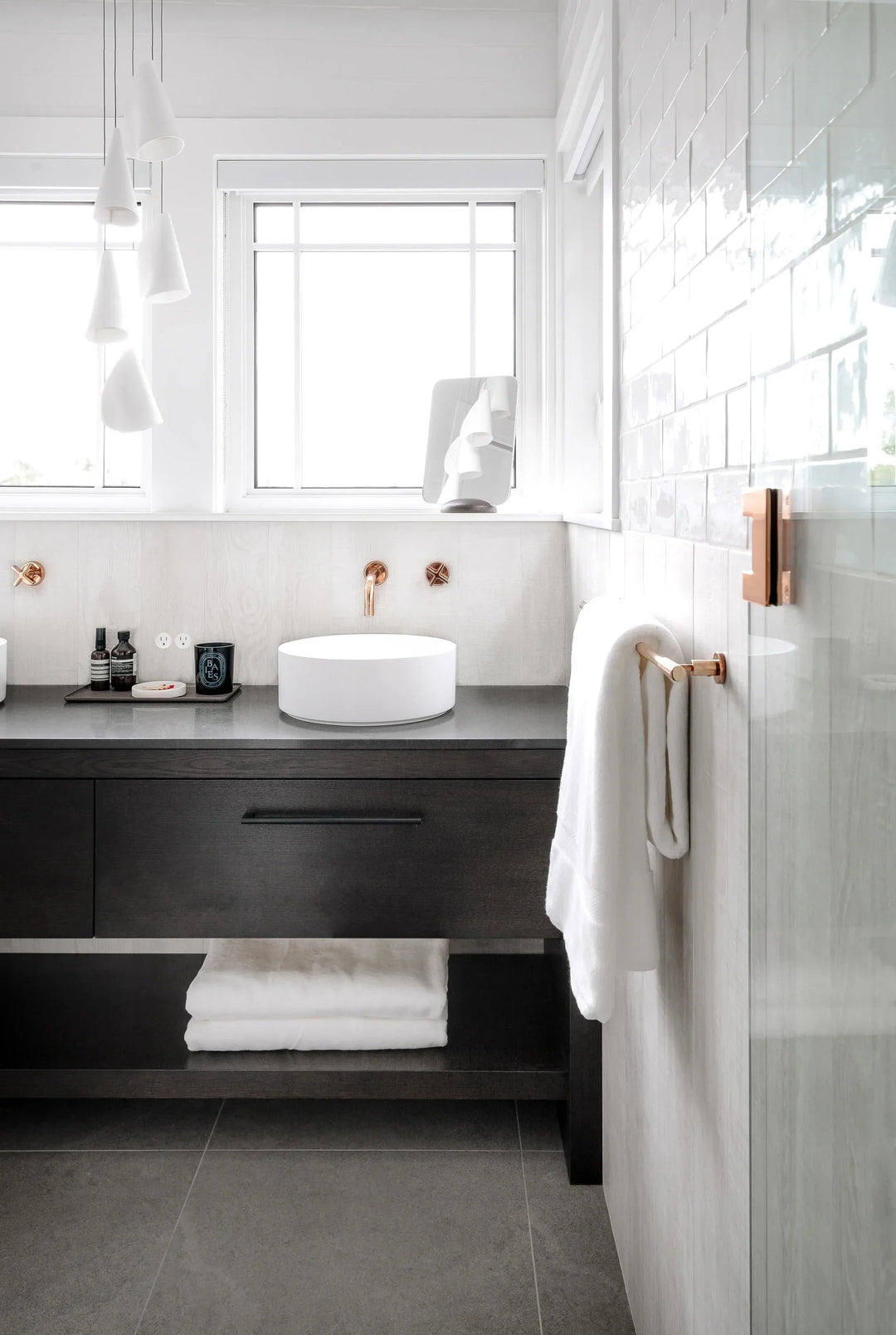 White folded-shade chandelier hangs beside bathroom windows above a dark vanity with a round white basin.