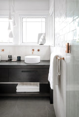 White folded-shade chandelier hangs beside bathroom windows above a dark vanity with a round white basin.