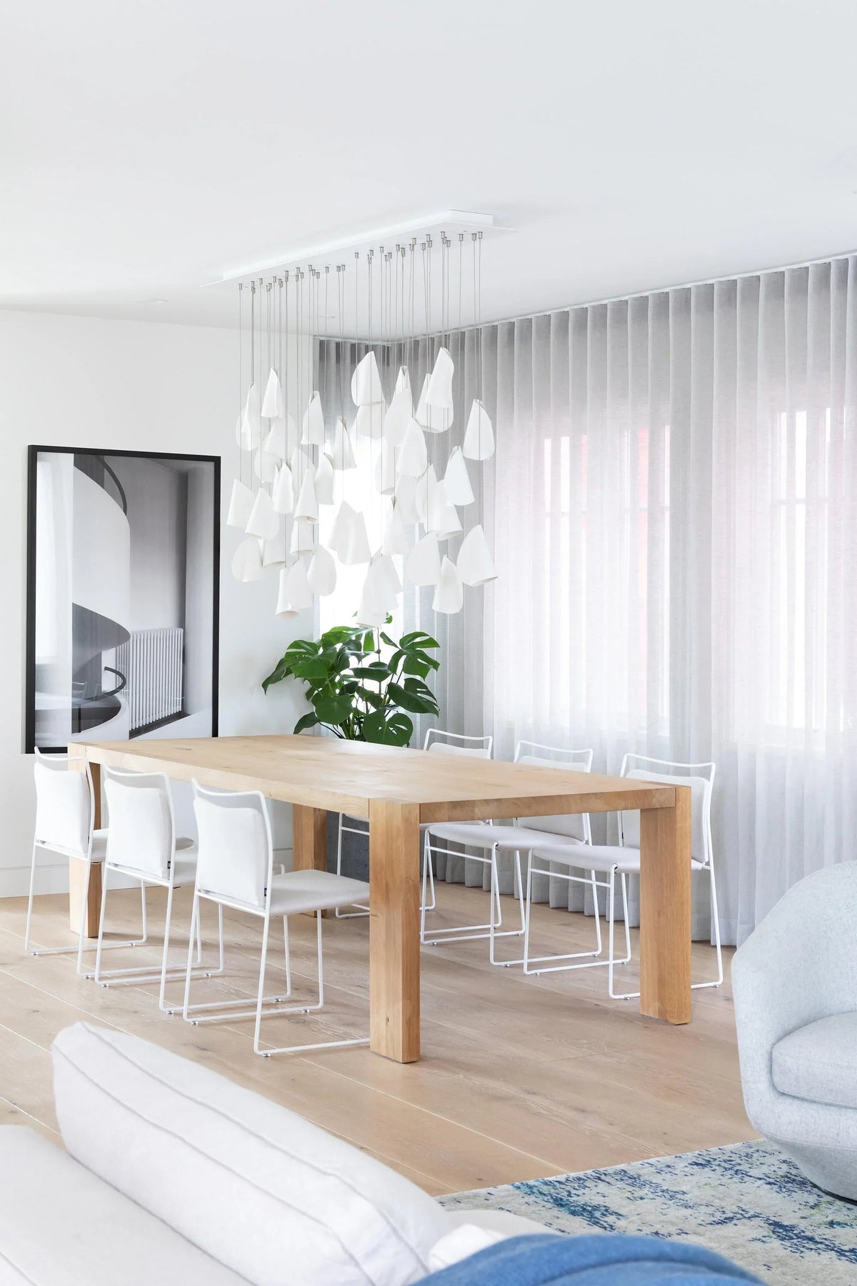 Modern dining room with a wooden table, white chairs, and decorative chandelier.
