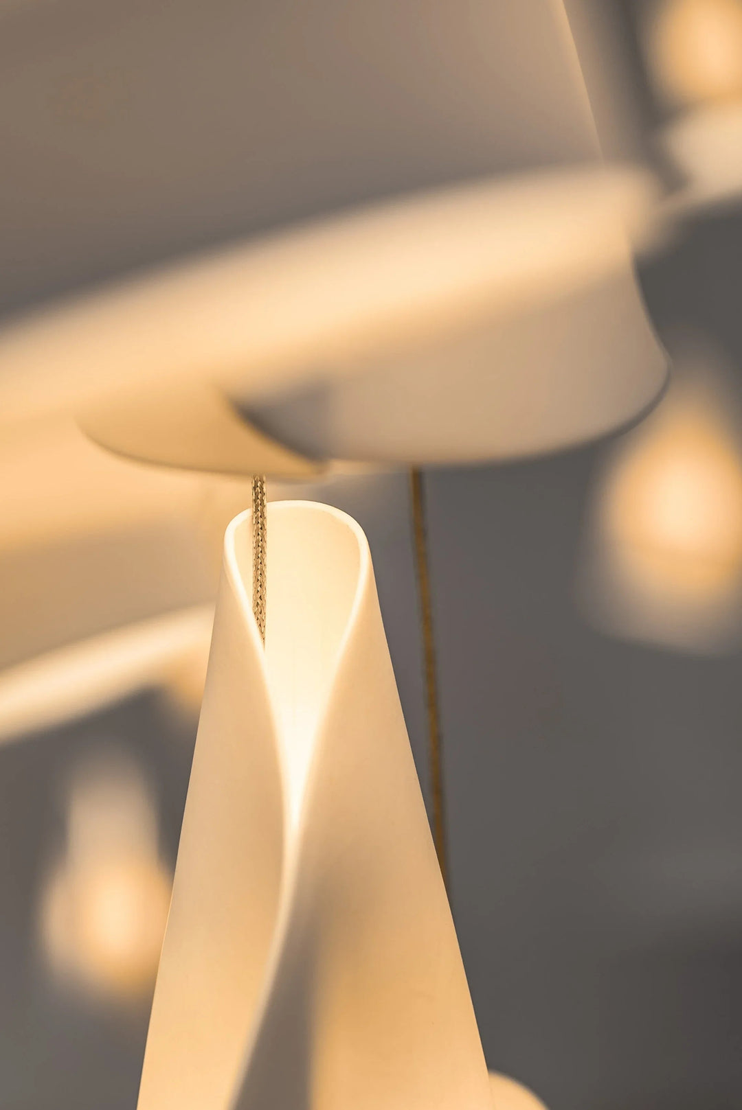 Close-up of a chandelier’s white porcelain shades showing curved folds, suspension cords, and softly glowing surfaces.