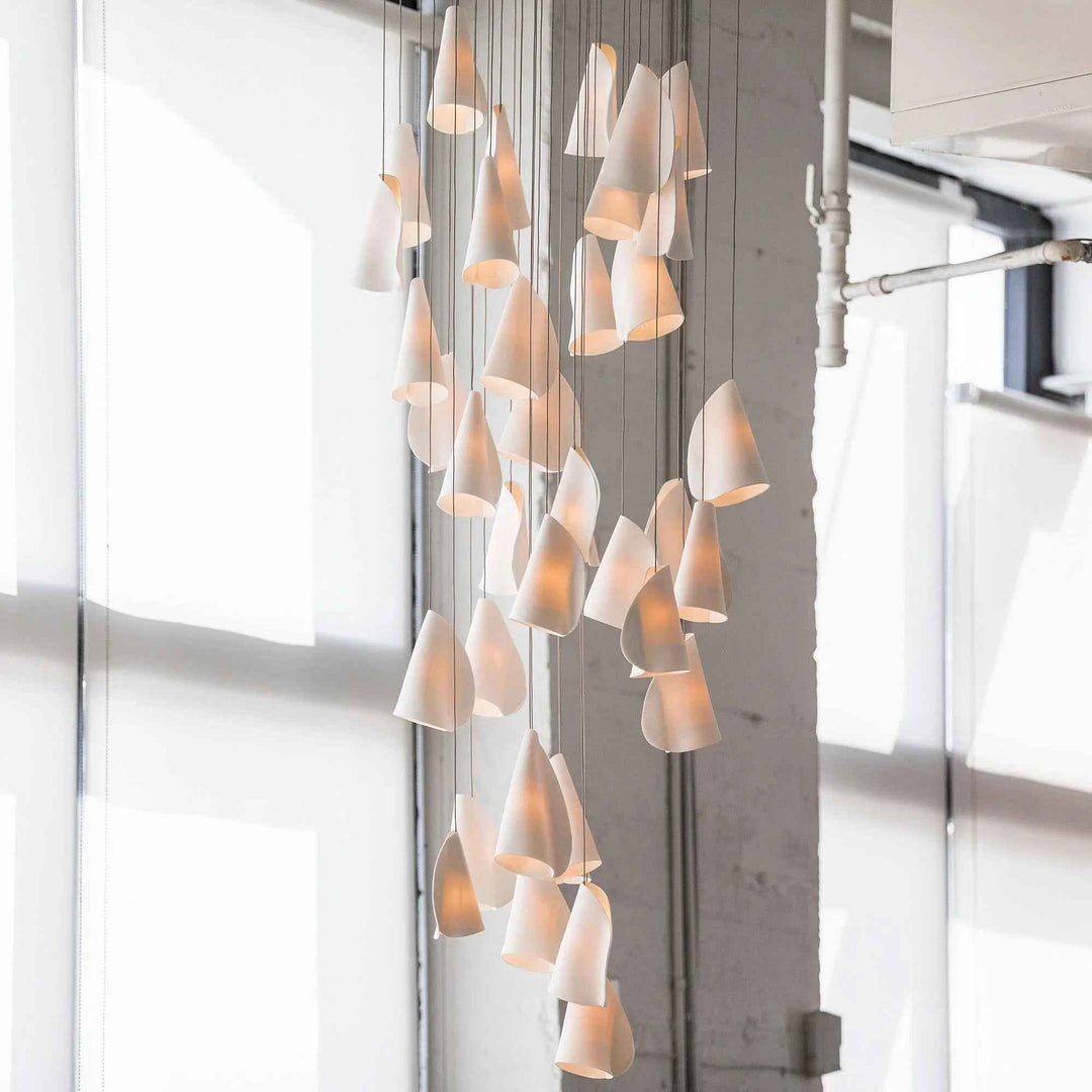 Modern chandelier with multiple lampshades in a room with large windows.