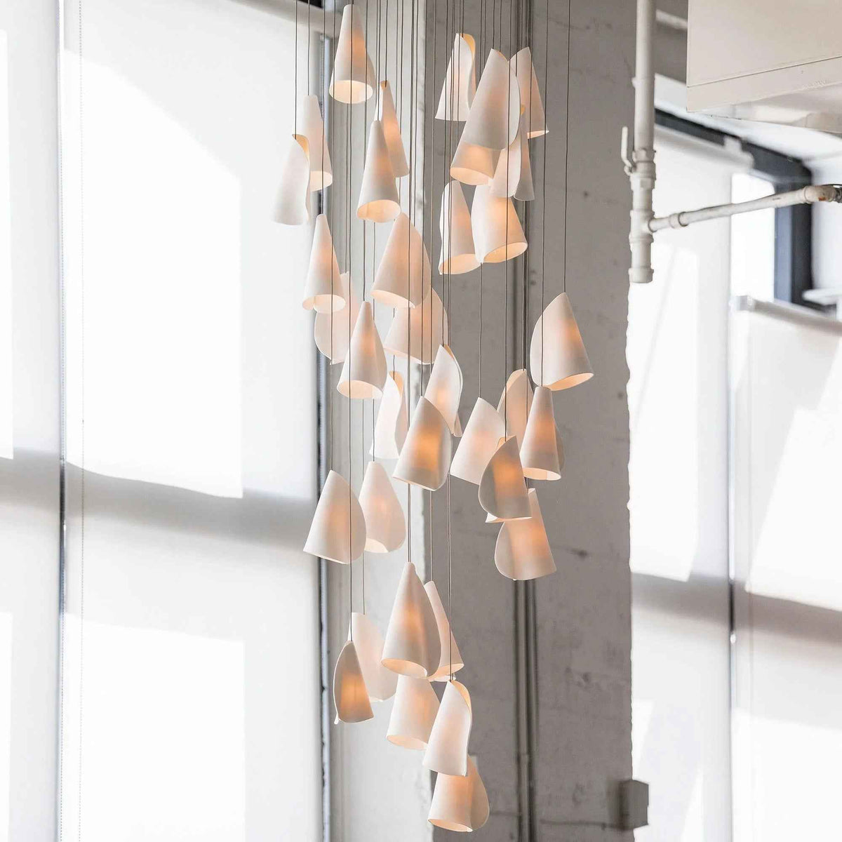 Modern chandelier with multiple lampshades in a room with large windows.