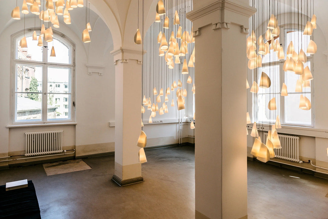 White porcelain chandelier clusters glowing between large columns in a high-ceilinged room with arched windows.