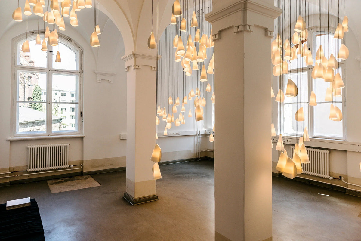 White porcelain chandelier clusters glowing between large columns in a high-ceilinged room with arched windows.