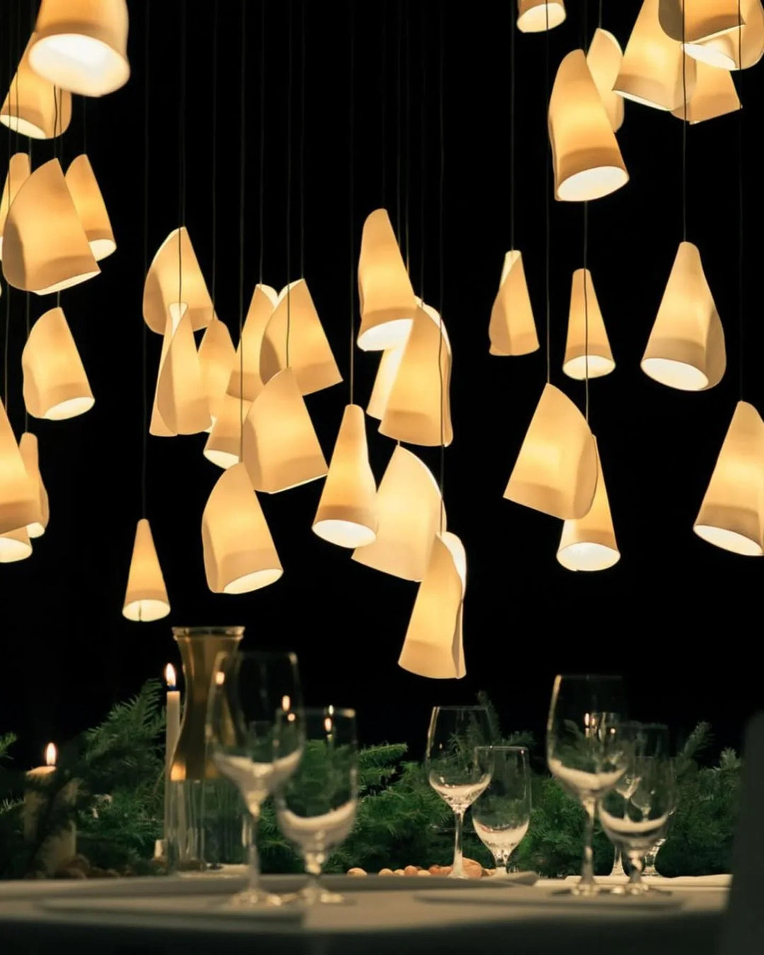 Chandelier with cone-shaped lights over a dining table with wine glasses.