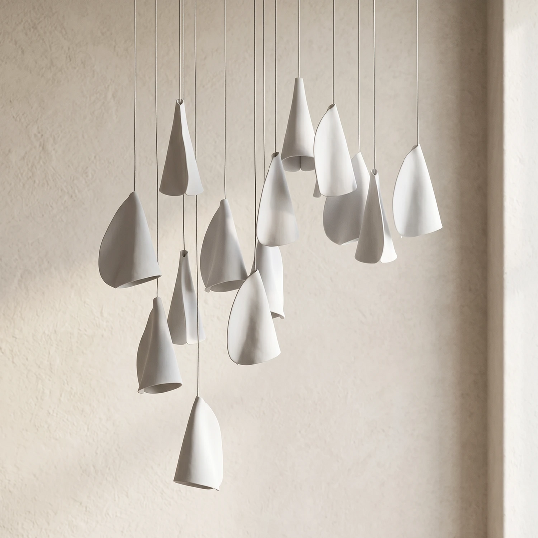 A modern multi-light pendant chandelier with teardrop-shaped white ceramic shades hanging from thin cables against a textured beige wall.